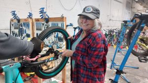 Woman with a had and plaid shirt working on a bike.